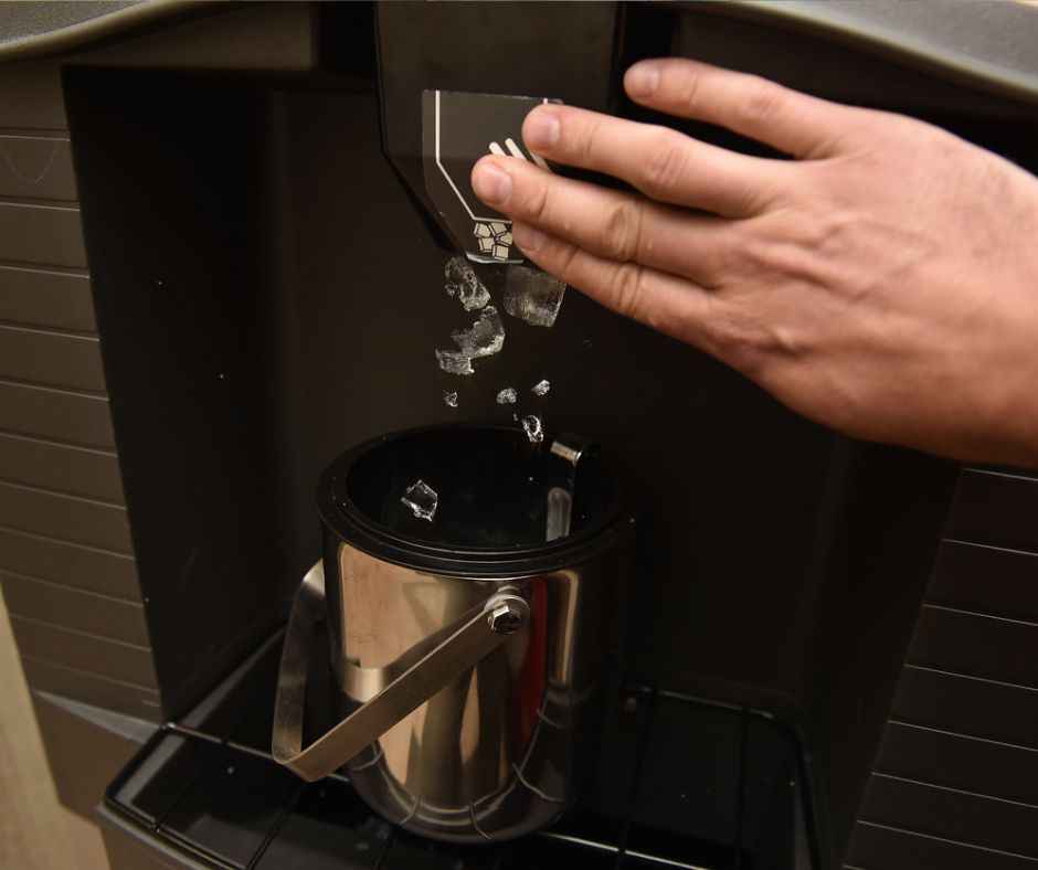 The hand of an adult male pressing an ice dispenser chute to dispense ice into a mug.